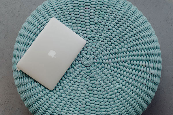 Ein Apple Laptop liegt auf einem blauen Pouf mit Innenhülle aus Strickwolle