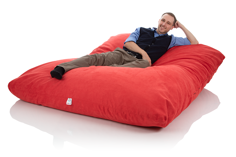 Junger Mann liegt in einem riesigen XXL-Sitzsack Bodenkissen rot der Groeße 140x180 cm