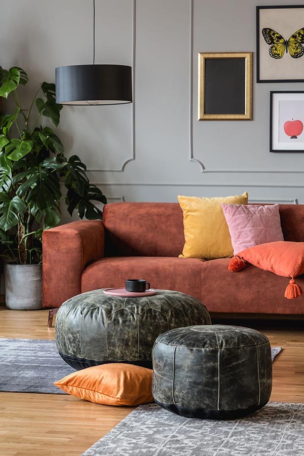 Zwei Leder Poufs verschiedener Größen stehen in einem Wohnzimmer vor einem Sofa
